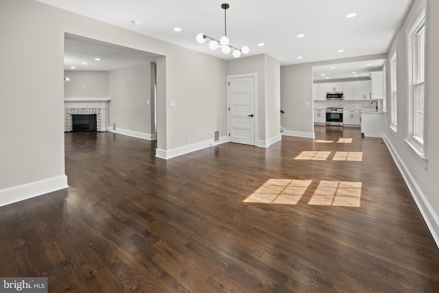 unfurnished living room featuring a brick fireplace, dark wood-style floors, baseboards, and a sink