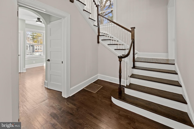 stairway with arched walkways, ceiling fan, baseboards, and wood finished floors