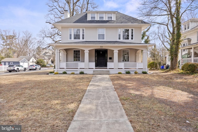 american foursquare style home with covered porch, roof with shingles, and stucco siding