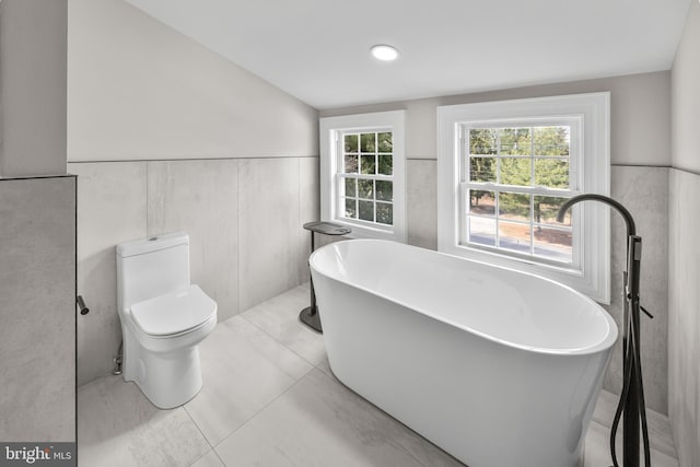 full bath with tile patterned flooring, wainscoting, a freestanding bath, and toilet