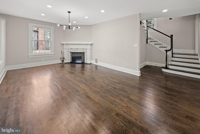 unfurnished living room featuring a brick fireplace, dark wood-type flooring, baseboards, stairs, and recessed lighting