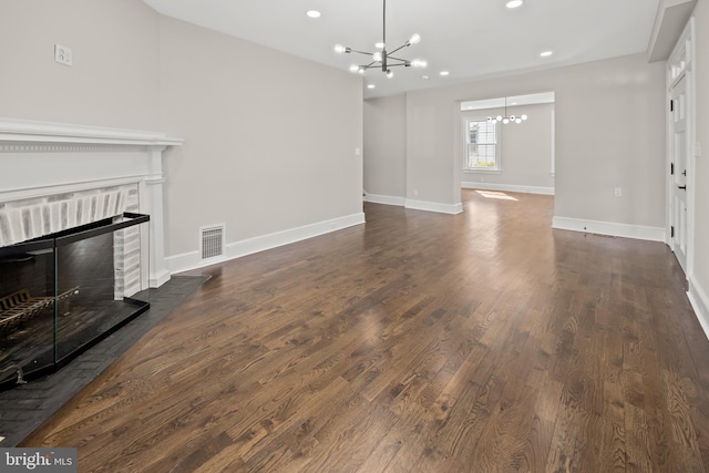 unfurnished living room featuring visible vents, wood finished floors, an inviting chandelier, baseboards, and a brick fireplace