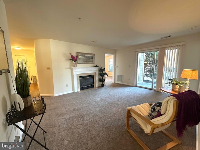 carpeted living area with a fireplace with flush hearth, baseboards, and visible vents