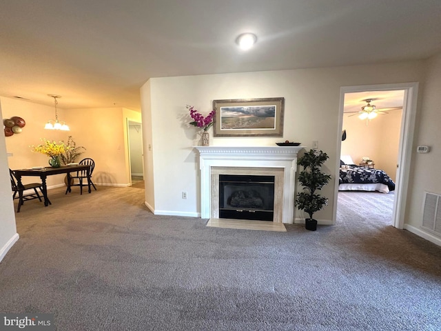 living area with visible vents, a fireplace with flush hearth, a notable chandelier, carpet floors, and baseboards