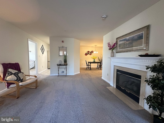 living area featuring a fireplace with flush hearth, baseboards, carpet, and an inviting chandelier