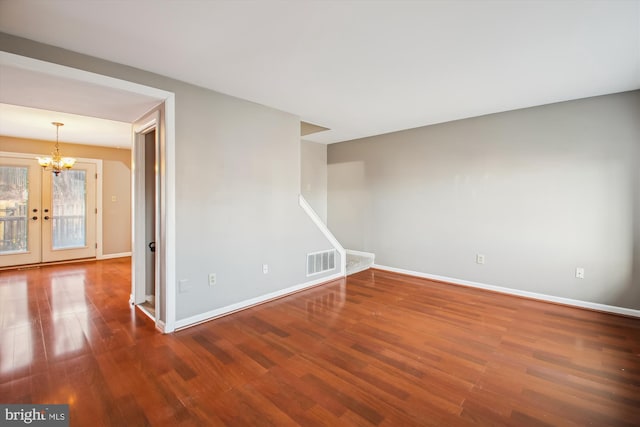 spare room featuring a notable chandelier, wood finished floors, visible vents, and baseboards