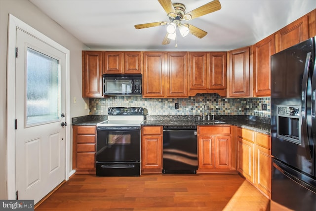 kitchen with black appliances, dark wood-style floors, tasteful backsplash, and a sink