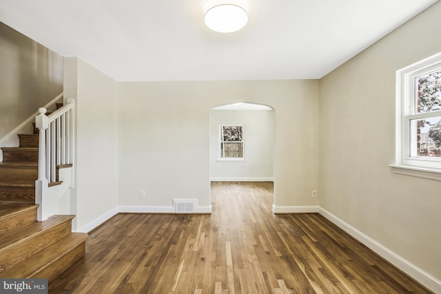 unfurnished room featuring stairway, wood finished floors, visible vents, baseboards, and arched walkways