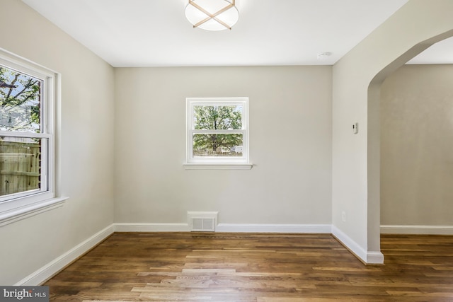 unfurnished room with wood finished floors, a healthy amount of sunlight, and arched walkways