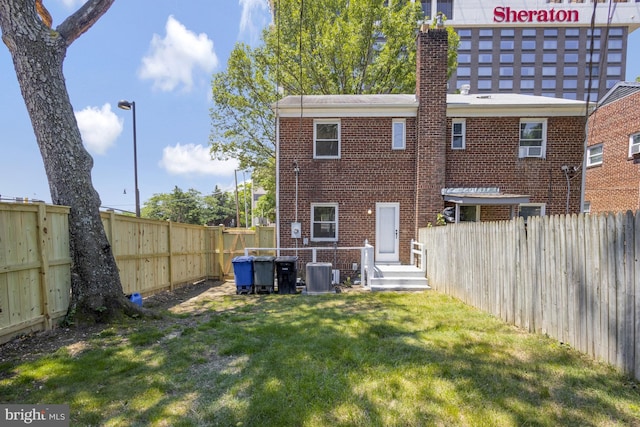 rear view of house featuring central air condition unit, a lawn, brick siding, and a fenced backyard