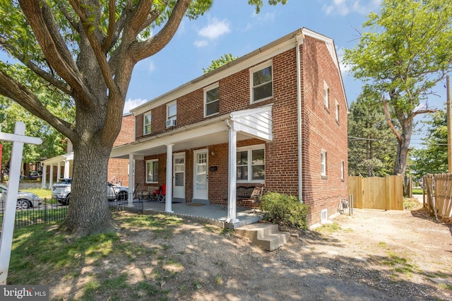 view of front of home with brick siding, covered porch, and fence