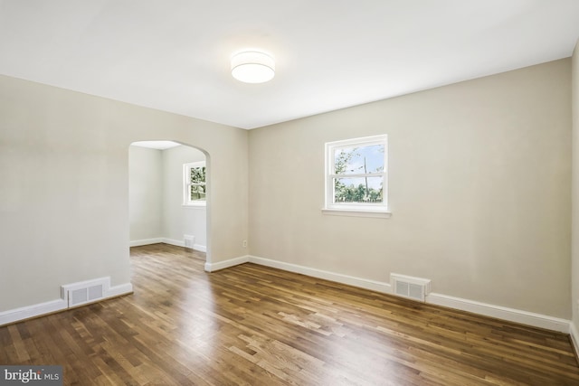 empty room featuring visible vents, arched walkways, baseboards, and wood finished floors