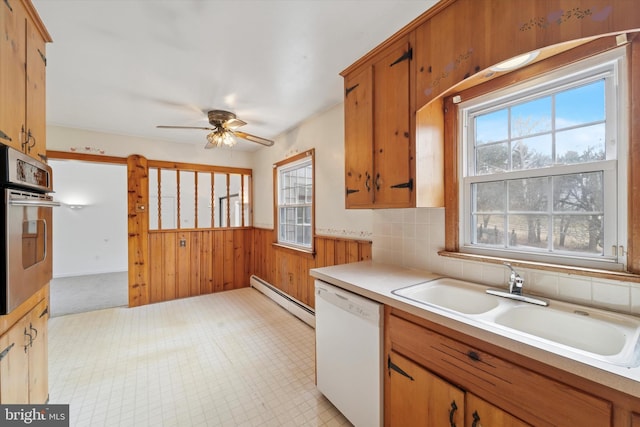 kitchen with a sink, wood walls, stainless steel oven, white dishwasher, and a baseboard radiator