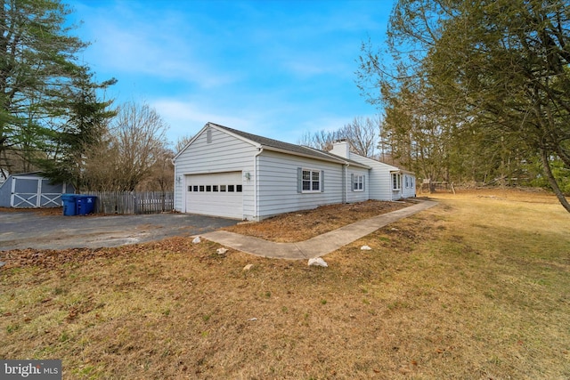 view of property exterior featuring fence, a lawn, a chimney, a storage shed, and an attached garage