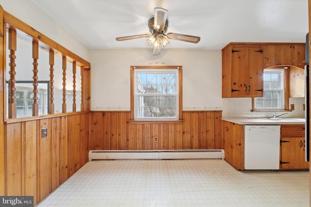 kitchen with wooden walls, a wainscoted wall, white dishwasher, light countertops, and a baseboard heating unit