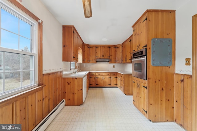 kitchen with wooden walls, light floors, a baseboard radiator, stainless steel oven, and a sink