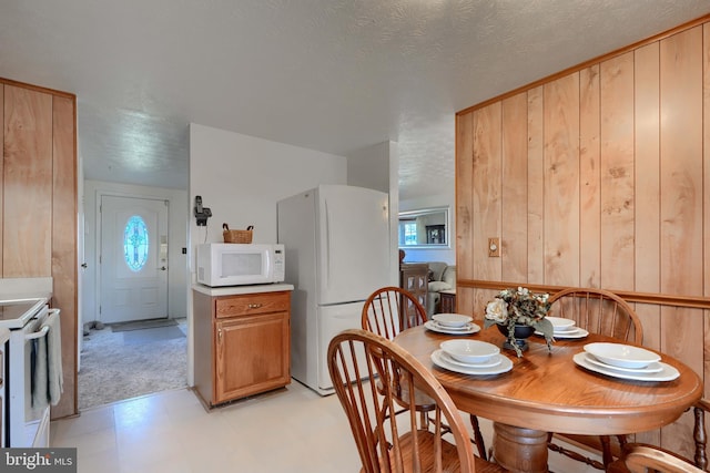 dining room with a textured ceiling, light floors, and wooden walls