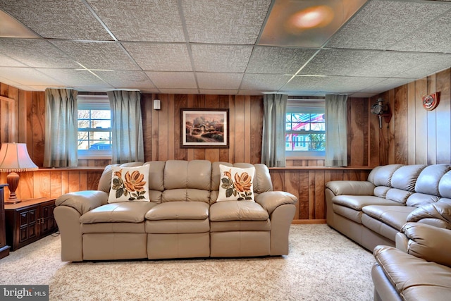 living area featuring light colored carpet, a paneled ceiling, and wooden walls