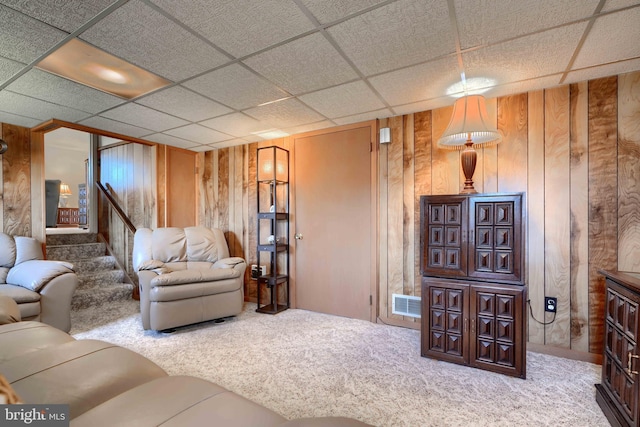 living area featuring a paneled ceiling, stairway, carpet floors, and wooden walls