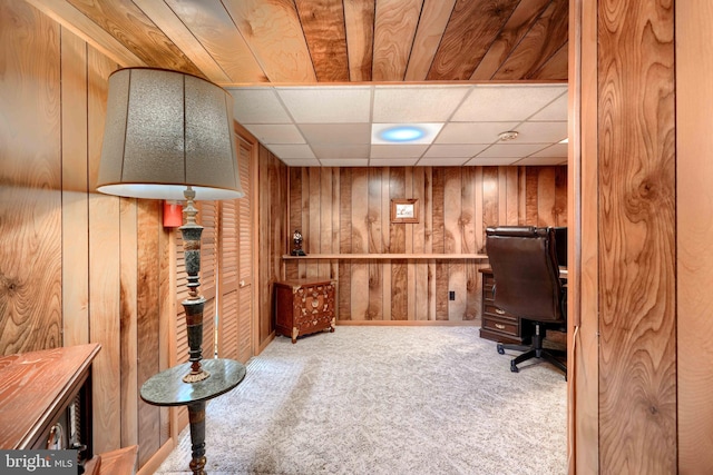 carpeted home office with wood walls and a paneled ceiling