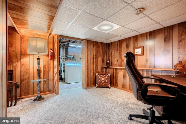 carpeted office featuring washer / clothes dryer, a paneled ceiling, and wood walls