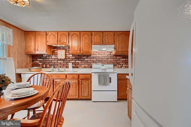 kitchen featuring under cabinet range hood, a sink, white appliances, brown cabinetry, and light countertops