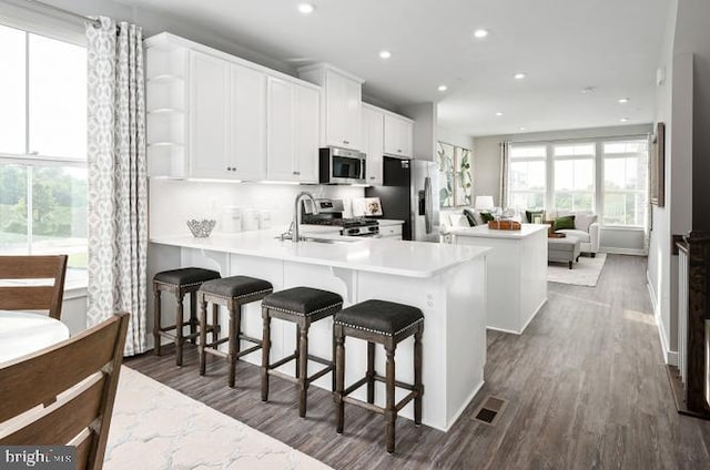 kitchen with a sink, a kitchen island, stainless steel appliances, a peninsula, and white cabinets