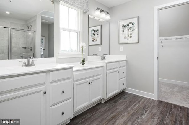 full bathroom with wood finished floors, baseboards, double vanity, a stall shower, and a sink