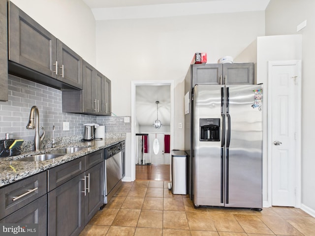 kitchen with light stone counters, light tile patterned flooring, a sink, decorative backsplash, and appliances with stainless steel finishes