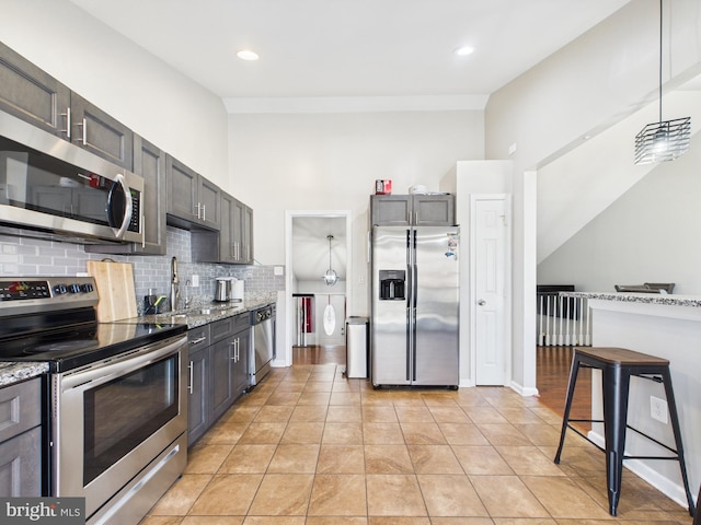 kitchen with light stone counters, decorative backsplash, light tile patterned flooring, stainless steel appliances, and a sink