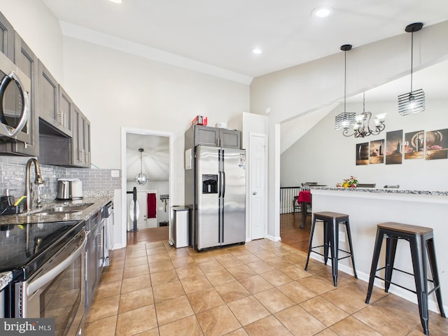 kitchen with light stone countertops, a sink, appliances with stainless steel finishes, pendant lighting, and backsplash