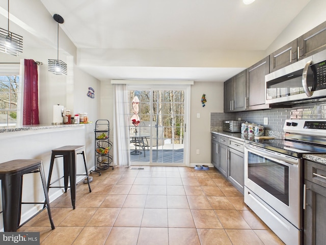 kitchen featuring light stone counters, tasteful backsplash, appliances with stainless steel finishes, light tile patterned floors, and hanging light fixtures