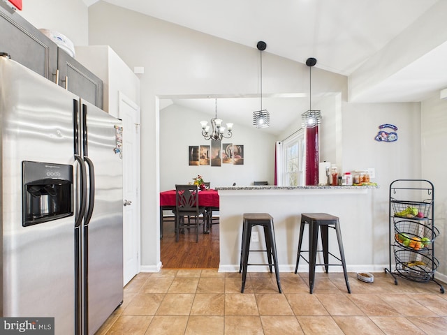 kitchen with light tile patterned floors, an inviting chandelier, vaulted ceiling, a kitchen breakfast bar, and stainless steel fridge