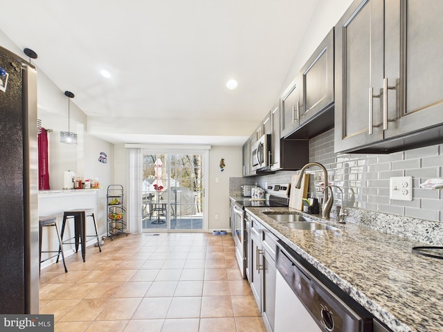 kitchen featuring light stone countertops, light tile patterned flooring, a sink, stainless steel appliances, and tasteful backsplash