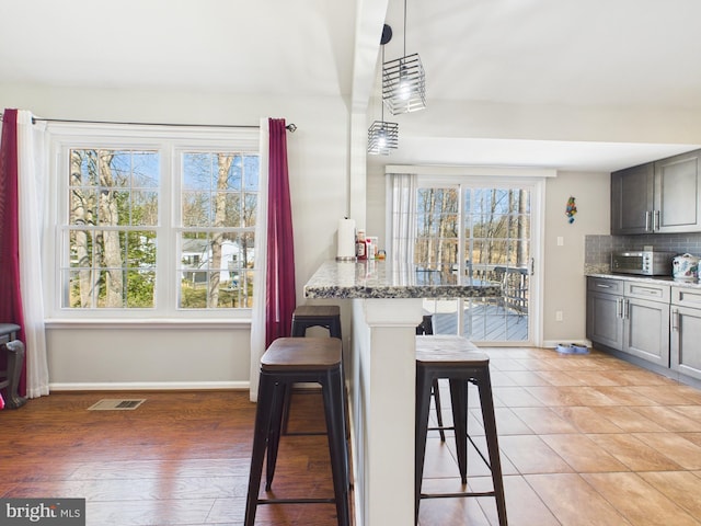 kitchen with light stone counters, visible vents, baseboards, a kitchen breakfast bar, and tasteful backsplash