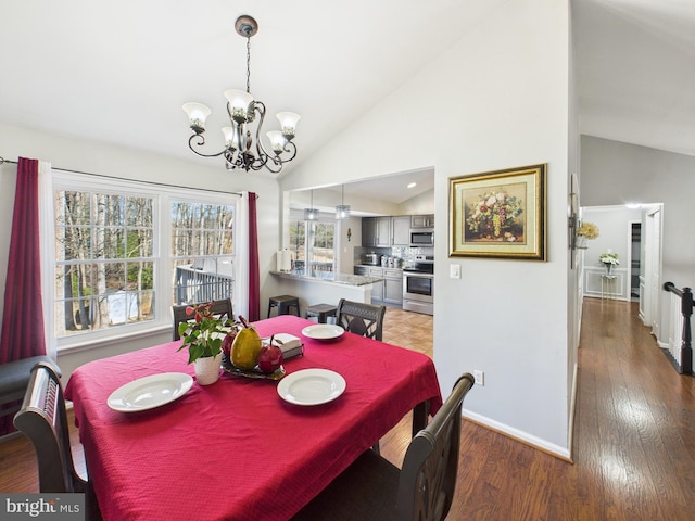 dining room featuring a chandelier, high vaulted ceiling, baseboards, and wood finished floors