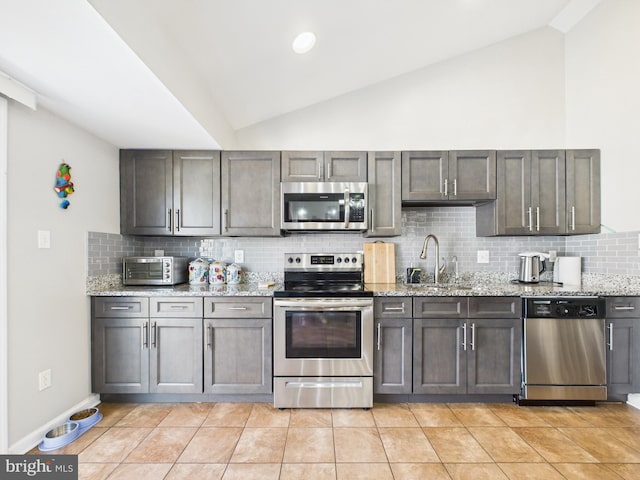 kitchen with light stone countertops, vaulted ceiling, light tile patterned floors, appliances with stainless steel finishes, and a sink