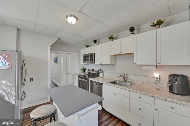 kitchen with appliances with stainless steel finishes, a kitchen breakfast bar, dark wood-style floors, white cabinets, and a sink