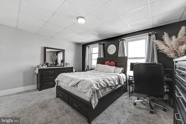 carpeted bedroom featuring baseboards and a drop ceiling