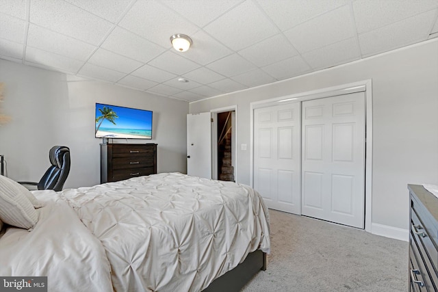 carpeted bedroom featuring a paneled ceiling, a closet, and baseboards