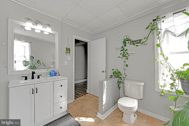 bathroom with baseboards, a drop ceiling, toilet, tile patterned floors, and vanity