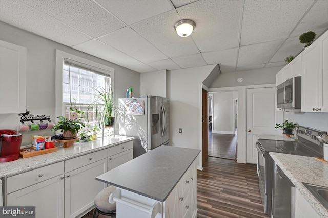 kitchen with a kitchen island, dark wood-type flooring, white cabinets, stainless steel appliances, and a paneled ceiling