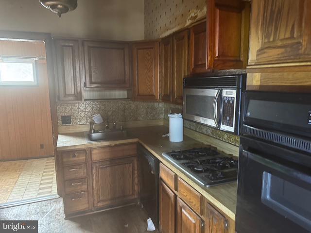 kitchen with decorative backsplash, black appliances, brown cabinetry, and a sink