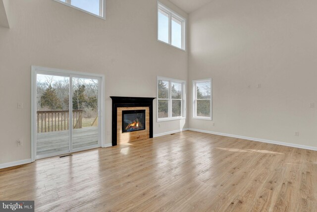 unfurnished living room with a tiled fireplace, visible vents, baseboards, and light wood-type flooring