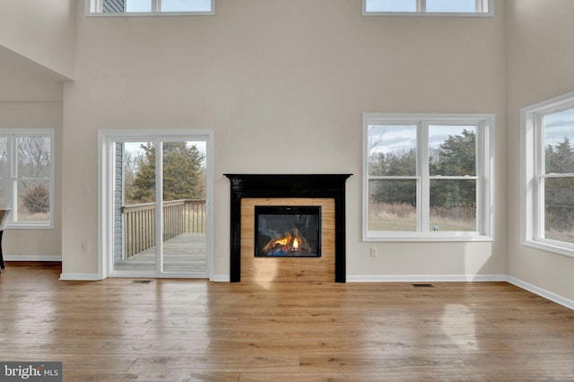 unfurnished living room with baseboards, a high ceiling, wood finished floors, and a glass covered fireplace