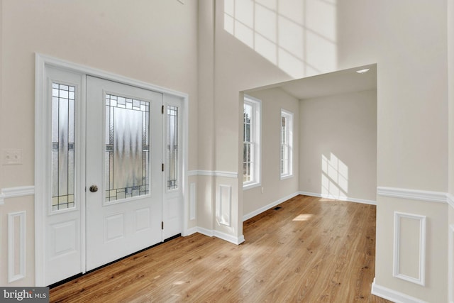 entrance foyer featuring baseboards, a towering ceiling, and light wood-type flooring