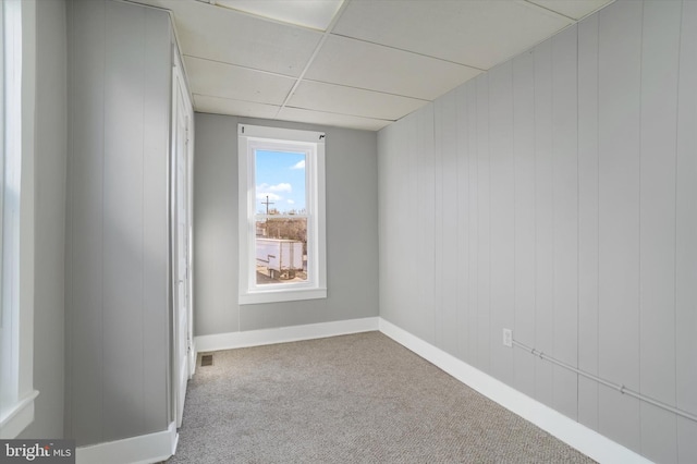 carpeted empty room featuring visible vents, baseboards, and a drop ceiling