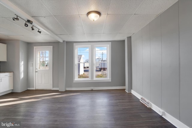 interior space featuring rail lighting, a healthy amount of sunlight, dark wood-style flooring, and a drop ceiling