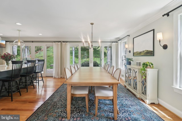 dining space featuring light wood-style floors, crown molding, baseboards, and a notable chandelier