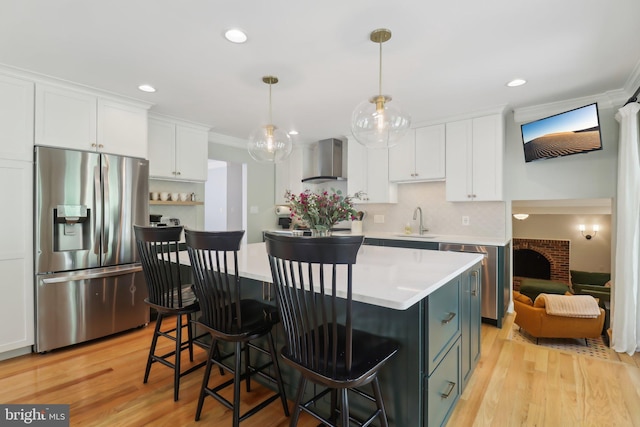 kitchen featuring light countertops, wall chimney range hood, a sink, stainless steel fridge, and white cabinetry